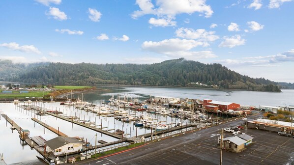 A marina with boats docked, a parking area, and a forested hill in the background.