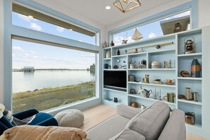 A modern living room with a large window overlooking a body of water, a flat-screen TV, and a collection of nautical-themed decor.