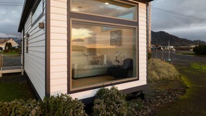 A modern, compact cabin with a large glass window, a sofa, and a chair inside. - Bayfront Tiny Home - Tillamook Bay/Garibaldi (Garibaldi)
