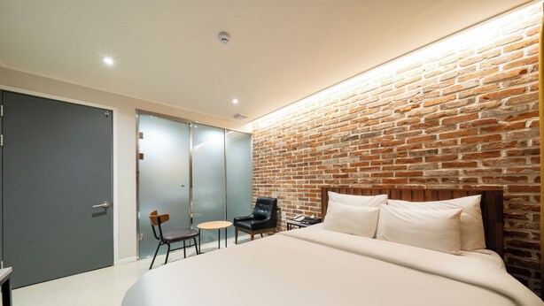 Une chambre d’hôtel moderne avec un grand lit, un mur décoratif en briques, une petite table, une chaise et une armoire.