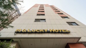 L’extérieur de l’hôtel M&Lucky présente un design moderne, avec une enseigne bien visible et une structure imposante dotée de nombreuses fenêtres.