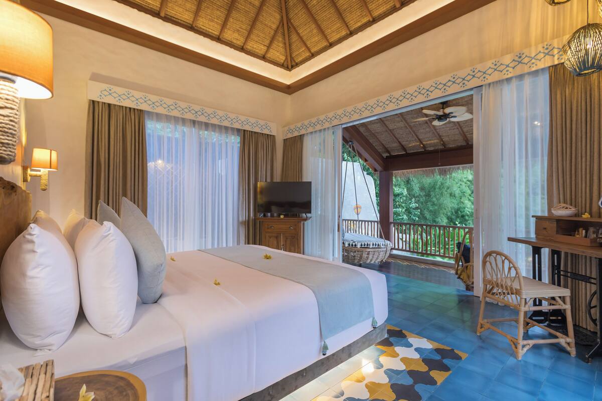 Habitación de hotel con cama, televisor, escritorio con silla y balcón con vistas a zonas verdes.