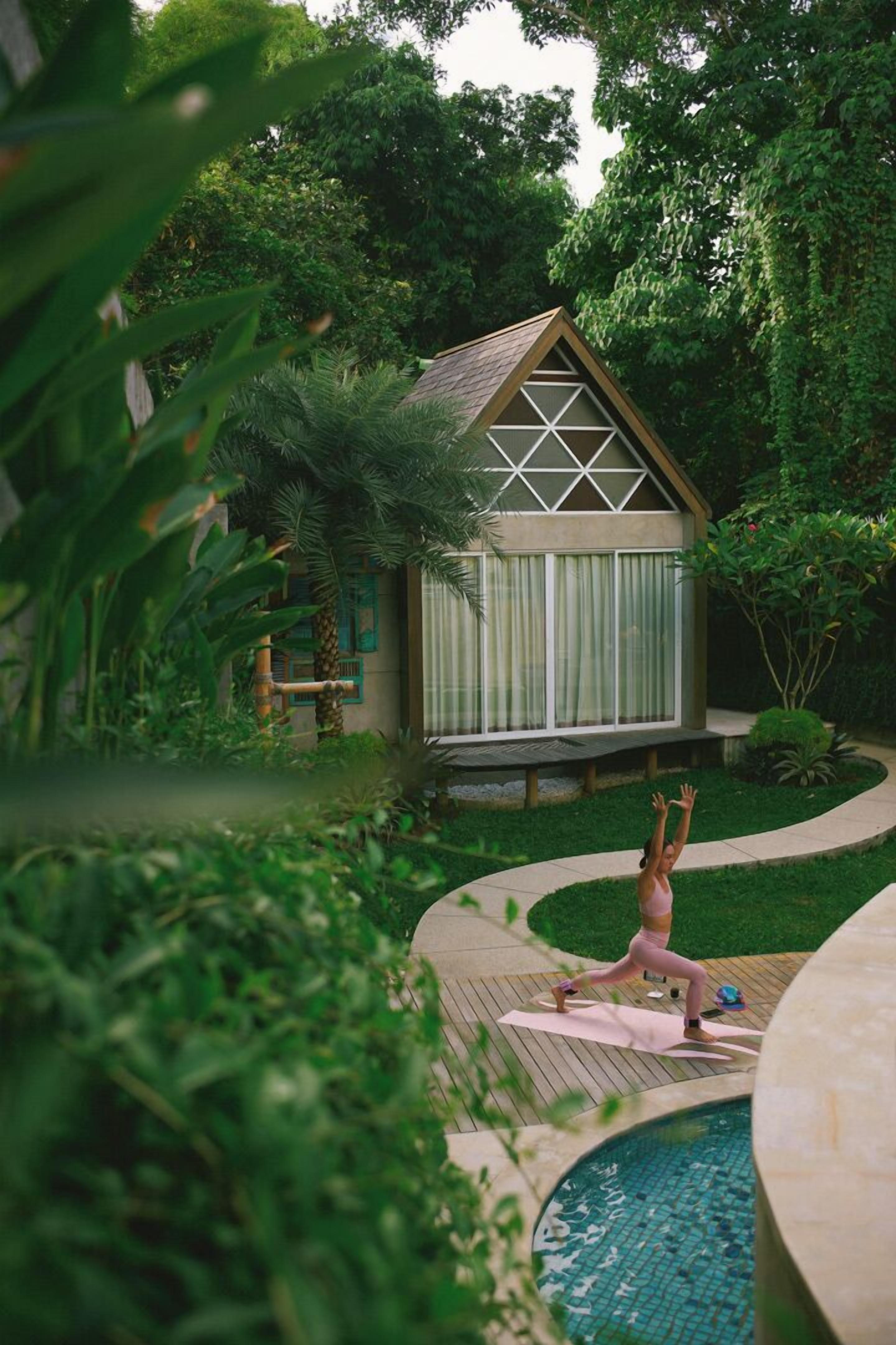 Een huis met een houten terras, een zwembad en weelderige begroeiing.
