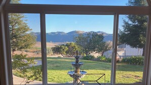 A dining area with a table and chairs, a view of a fountain, and a landscape with trees and mountains.