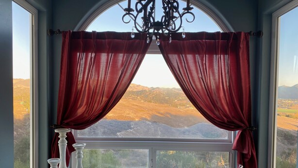 A room with a large window, red curtains, a chandelier, and a bathtub.