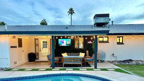 A poolside area with a covered seating area, a TV screen, and string lights.