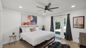 A modern bedroom with a bed, ceiling fan, artwork, and a view through the door.