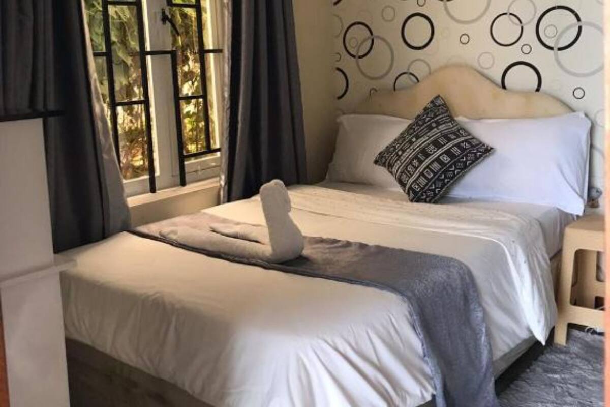 Quarto com cama, cortinas, parede estampada e janela com vista para o verde.