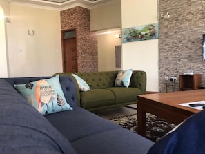 Una sala de estar con un sofá verde, un sofá oscuro y una mesa de centro de madera. Hay una pared de piedra y un cuadro en la pared.