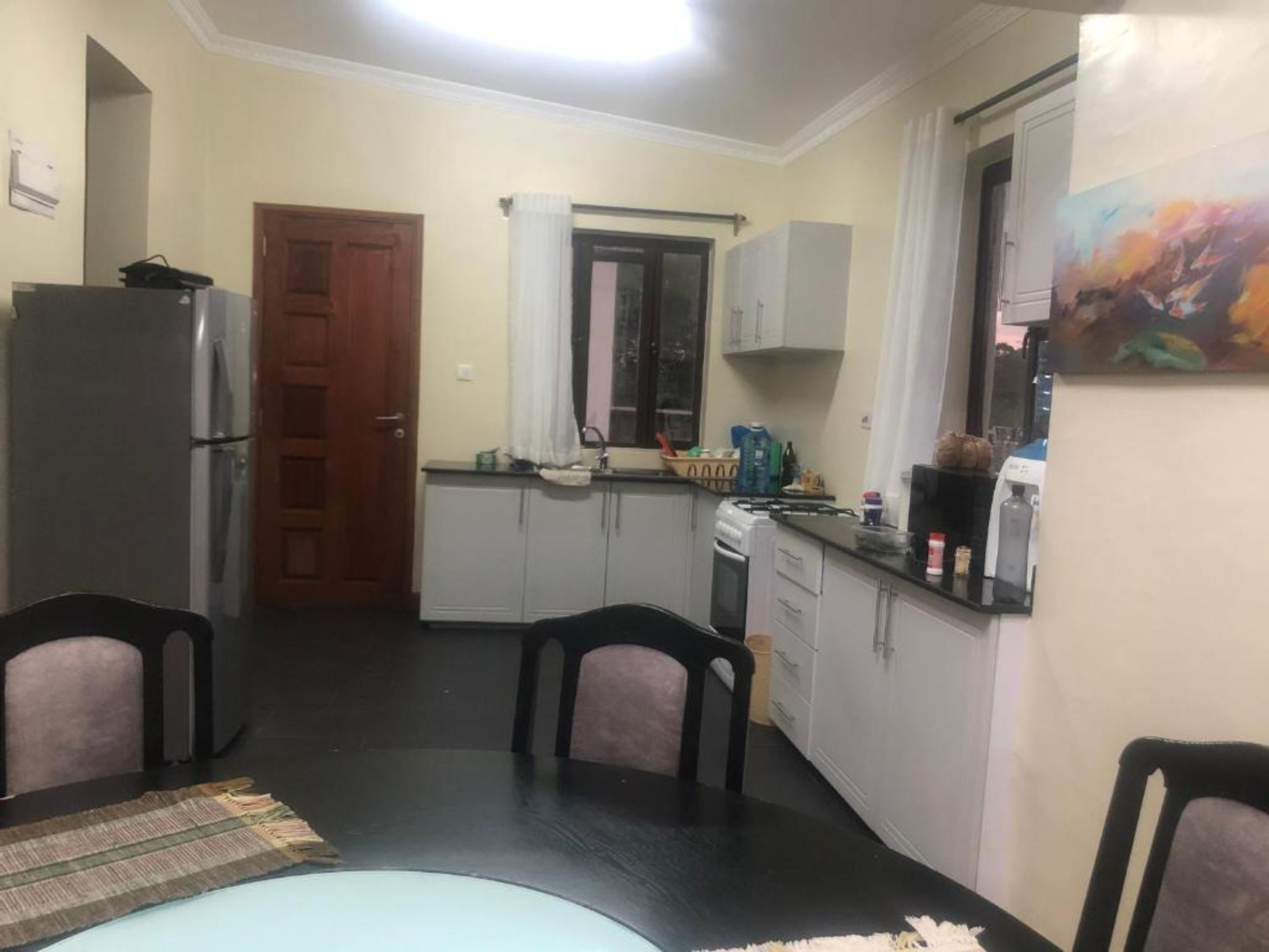 A compact kitchen with a refrigerator, stove, and sink. There are two chairs and a dining table.