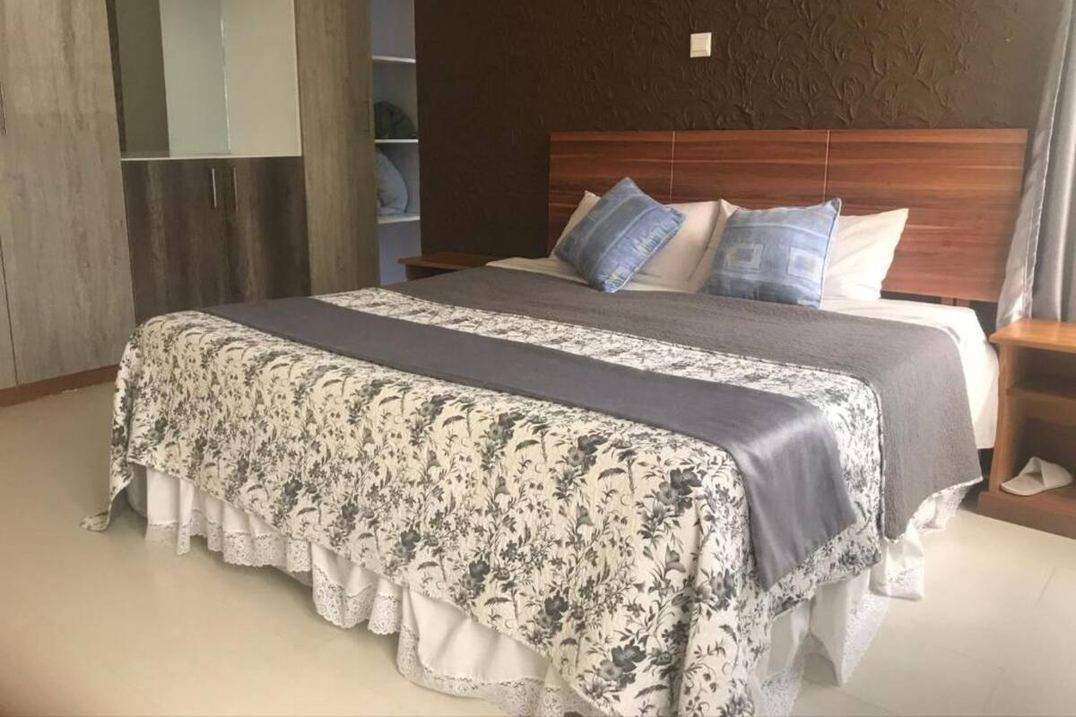 Uma cama bem arrumada com colcha e almofadas florais, uma cabeceira de madeira e um guarda-roupa com espelho.