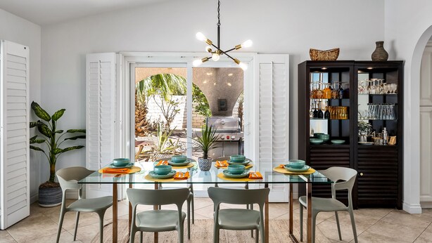 Un coin repas comprenant une table en verre, quatre chaises, un barbecue et un buffet sombre où sont rangés des verres.
