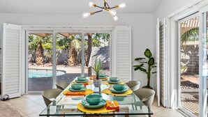 Un coin repas avec une table en verre, des chaises et une vue sur une piscine et un jardin.