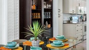 Un espace repas moderne avec une table en verre, des assiettes turquoise et orange, et une plante en pot.