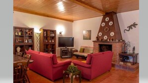 A cozy living room with a fireplace, red sofas, wooden shelves, and a flat-screen TV.