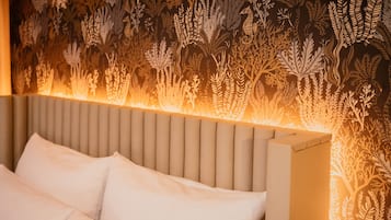 A bed with a headboard and pillows, set against a wall with a leaf-patterned wallpaper.