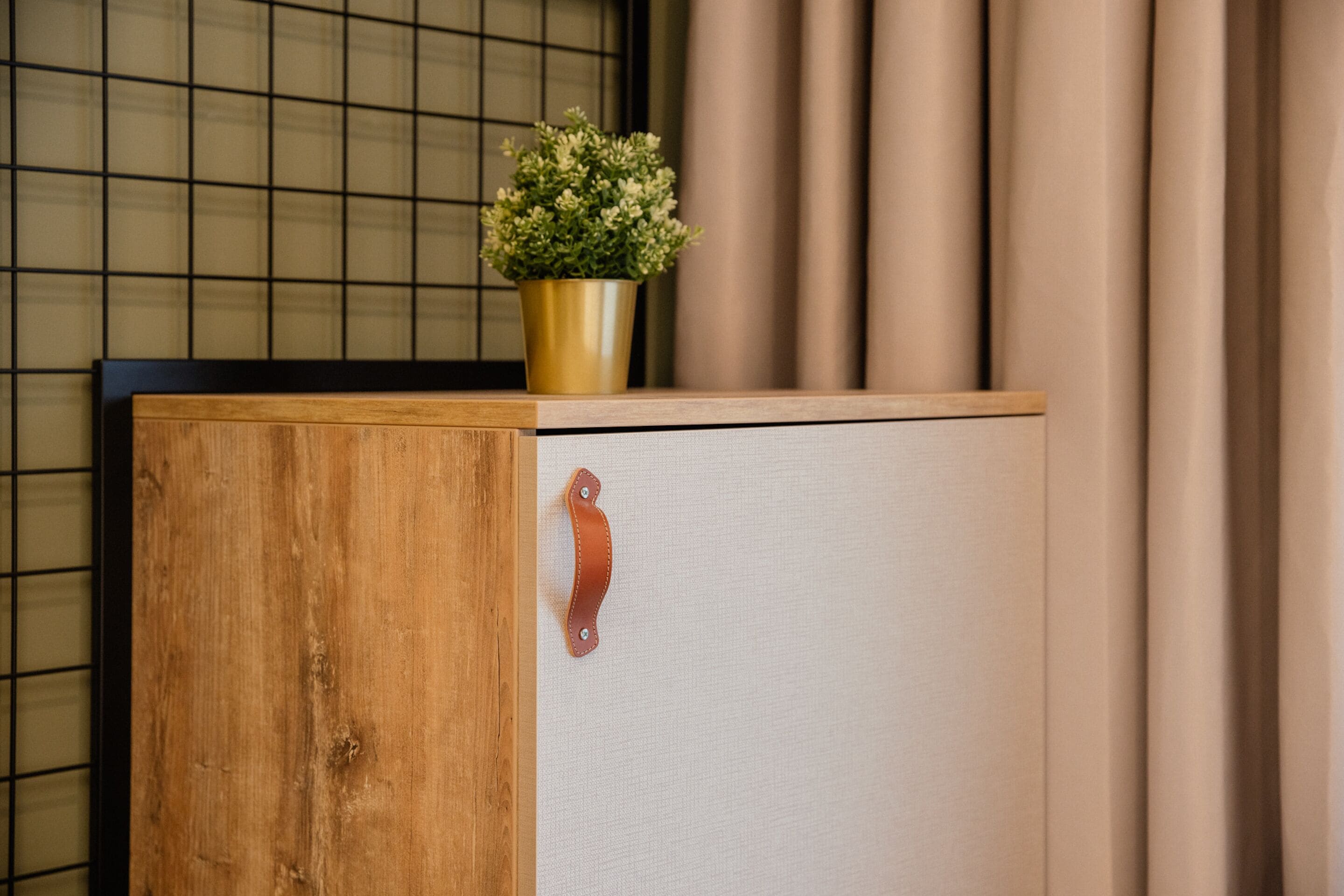 Een houten kastje met een metalen handgreep en een bloempotje erboven.
