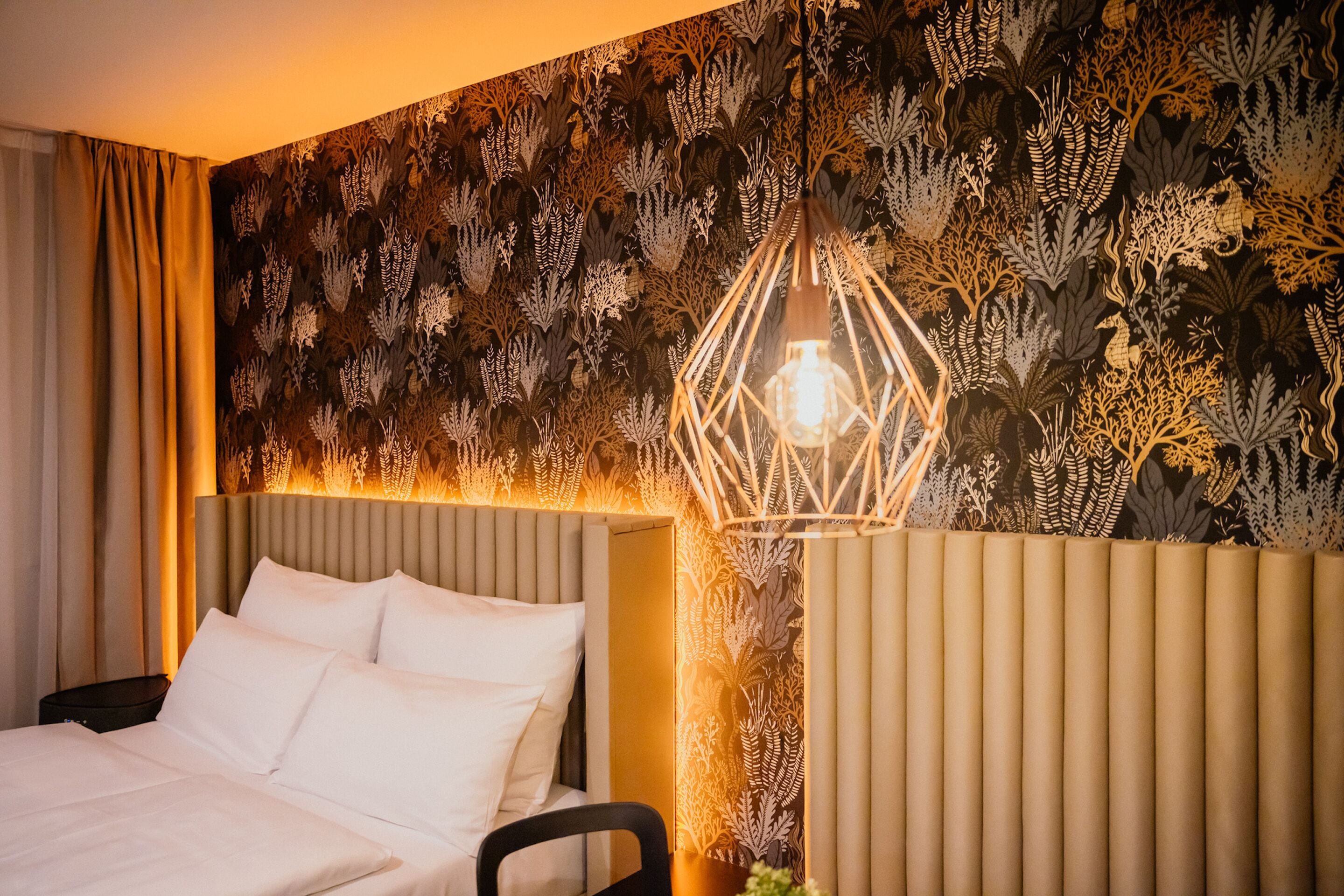 Ein Hotelzimmer mit einem Bett, einem Nachttisch und einer Wand mit einem Blattmuster.