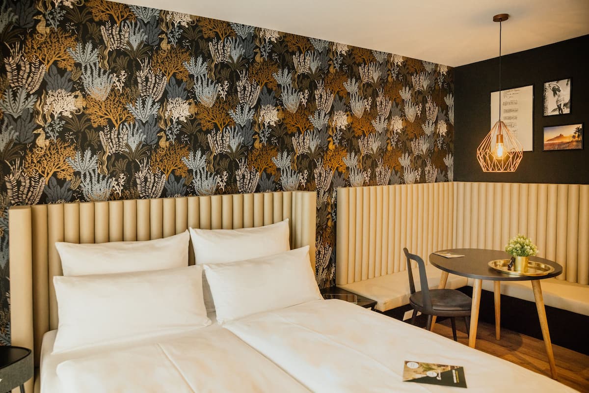 Habitación de hotel con cama, una mesa redonda con una silla, un banco y un papel tapiz con diseño.