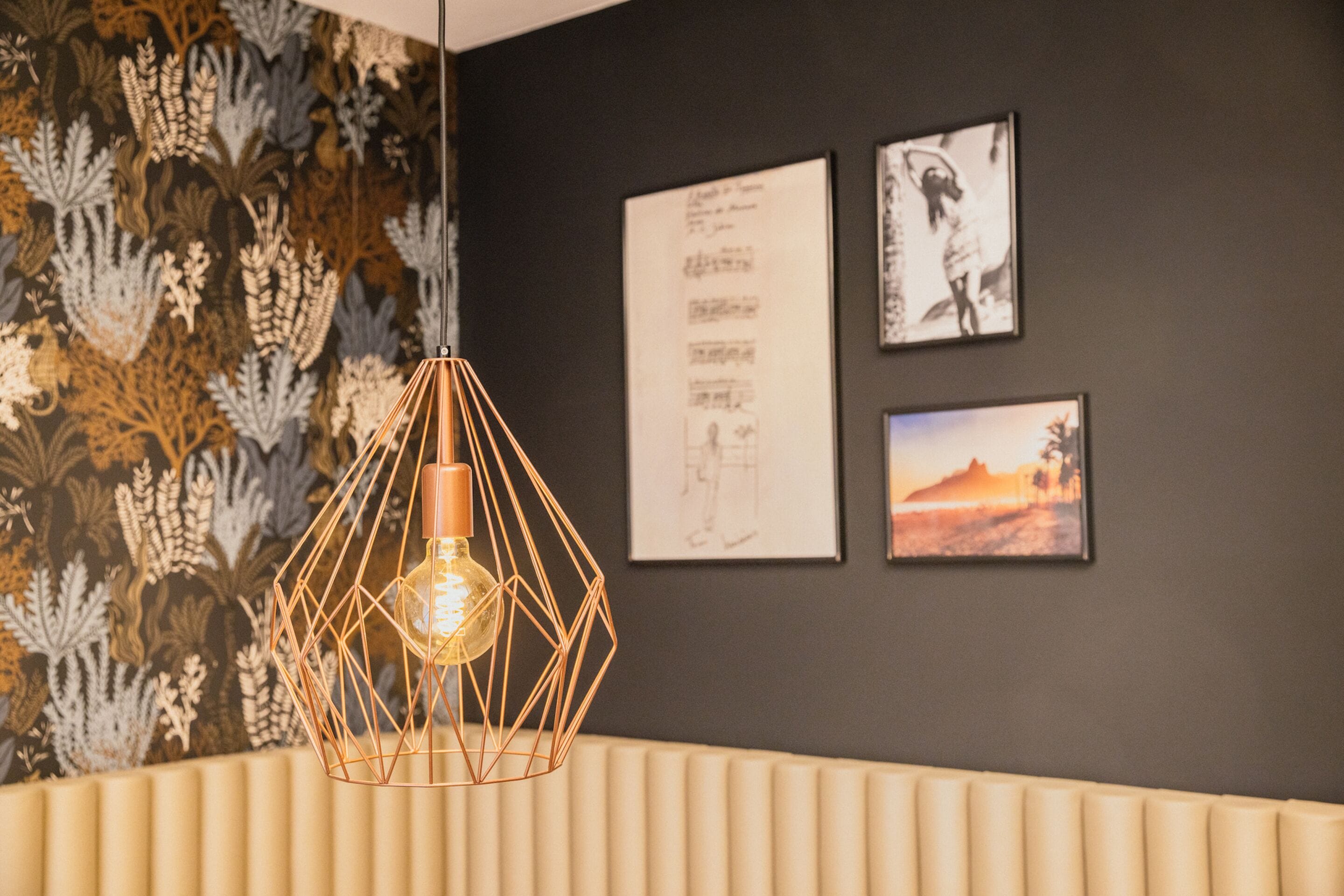 Un interior moderno con una lámpara colgante geométrica, un papel tapiz estampado y cuadros en la pared.