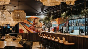 A bar area with a mural, wooden bar stools, and hanging lights. - Rioca Stuttgart Posto 4 (Stuttgart)