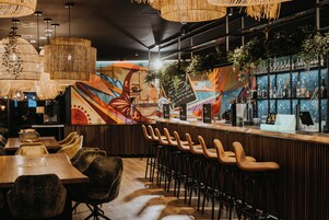 Zona de bar con un mural, taburetes de madera y luces colgantes.