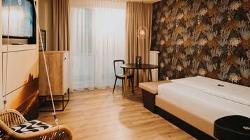 A modern hotel room with a wooden floor, a sofa, a dining table with chairs, a hanging chair, and a patterned wallpaper.