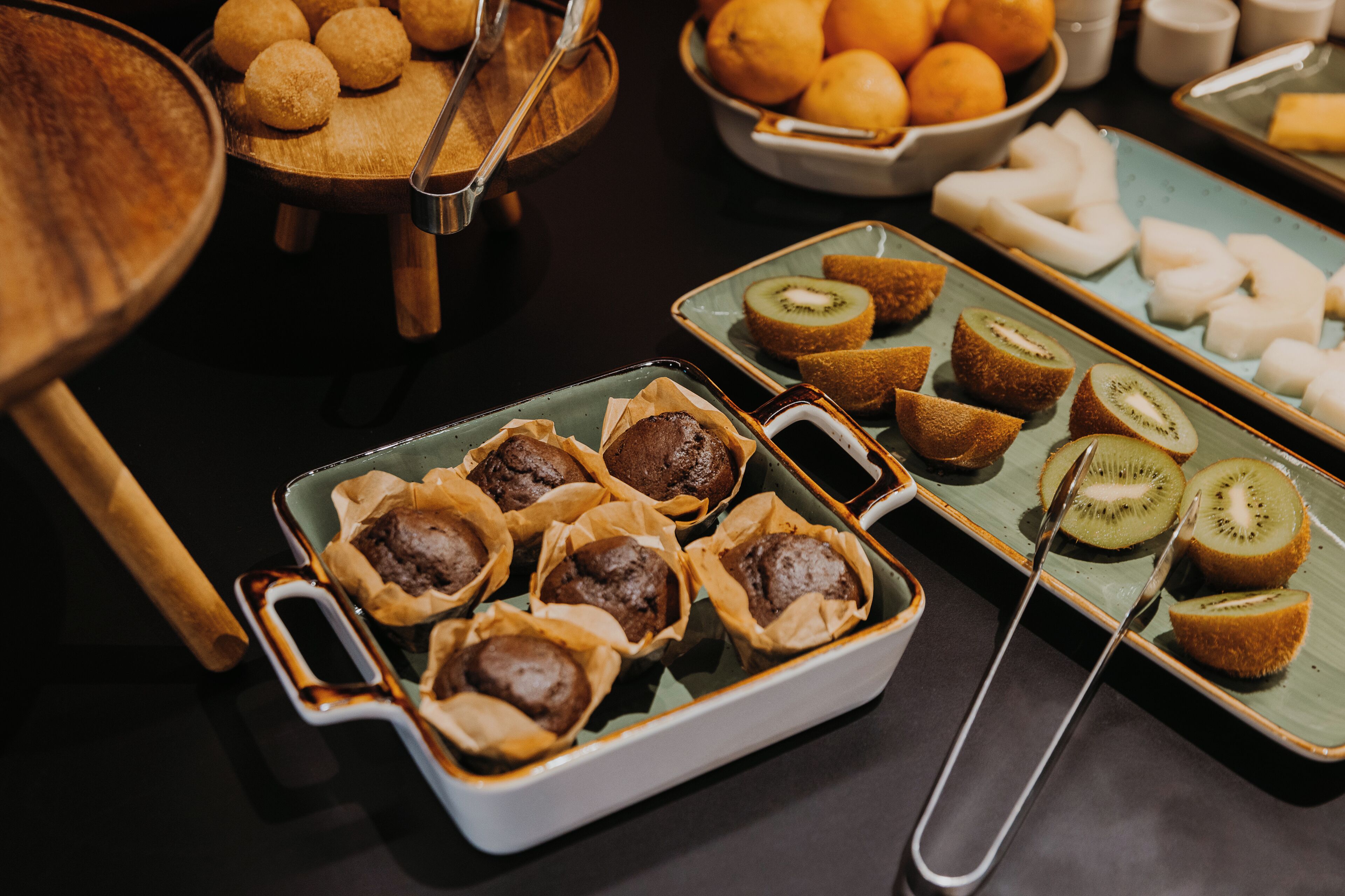 A buffet with various food items including muffins, kiwi slices, and oranges.