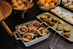A buffet with various food items including muffins, kiwi slices, and oranges.