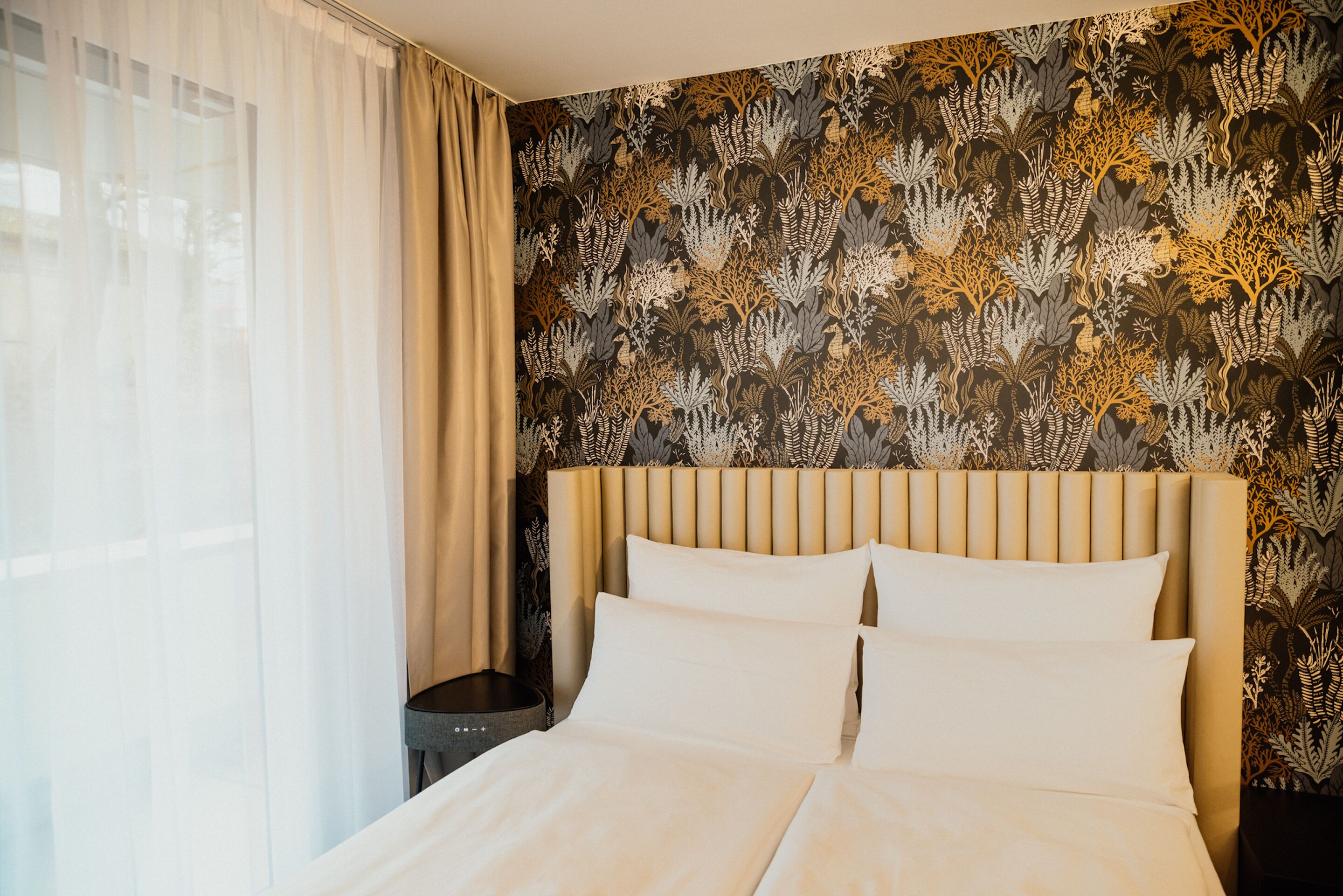 A hotel room with a bed, curtains, and a patterned wallpaper.