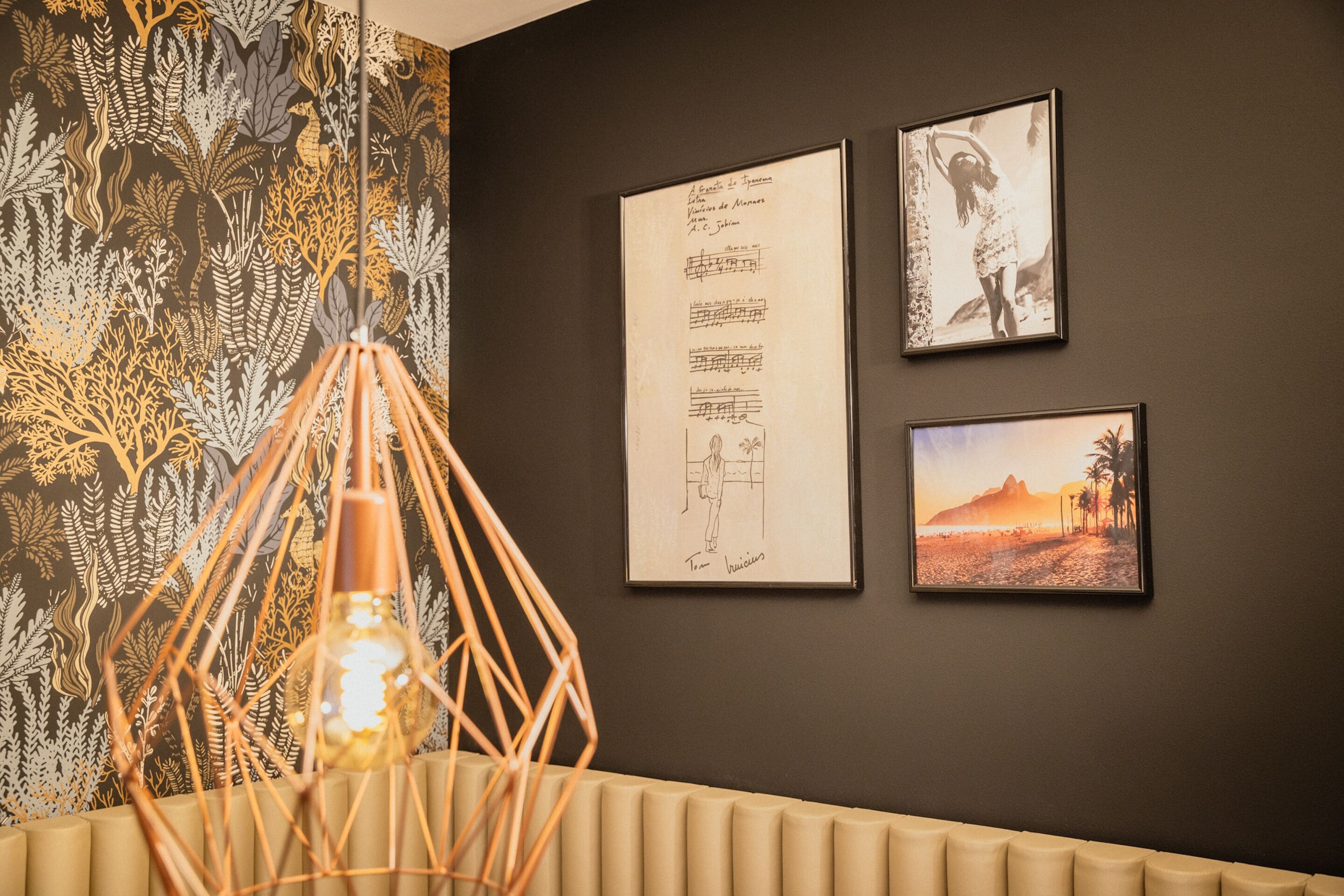 Una habitación con papel tapiz estampado, una lámpara colgante y tres obras de arte enmarcadas en la pared.