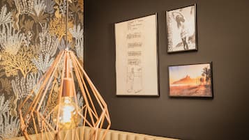 A room with a patterned wallpaper, a hanging light fixture, and three framed artworks on the wall.