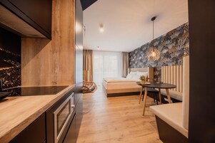 Un dormitorio moderno con suelo de madera, una cama, una mesita de noche, una lámpara colgante y vistas a la ciudad de noche.