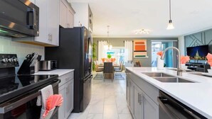 A modern kitchen with stainless steel appliances, a central island with a sink, and a dining area in the background. - Wonderful 5 Bd Private Pool at Storey Lake Resort (Kissimmee)