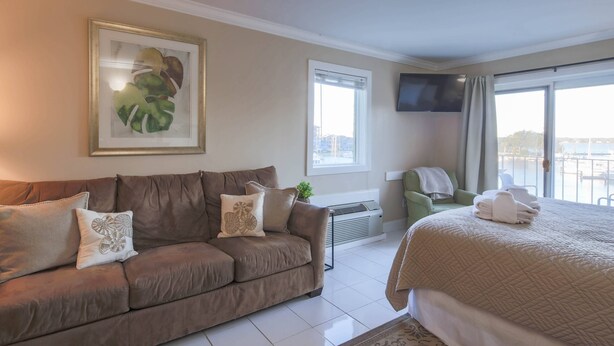 Une chambre d’hôtel avec un canapé marron, un lit recouvert d’une courtepointe, un téléviseur à écran plat, une fenêtre donnant sur un beau paysage et une petite table agrémentée d’une plante.