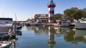 A marina with boats docked, a prominent red and white lighthouse, and a building with outdoor seating. - Spectacular Studio in the Heart of Harbour Town overlooking Harbour & Lighthouse. Dine, Shop, Relax. (Hilton Head Island)