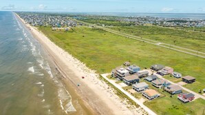 Vue aérienne d’une zone résidentielle côtière, avec des maisons le long de la plage et une route qui longe le rivage.