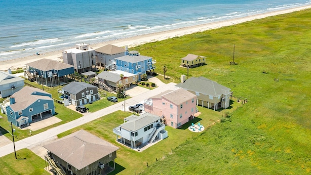 Vue aérienne d’une zone résidentielle côtière, avec des maisons, une plage et un ciel dégagé.