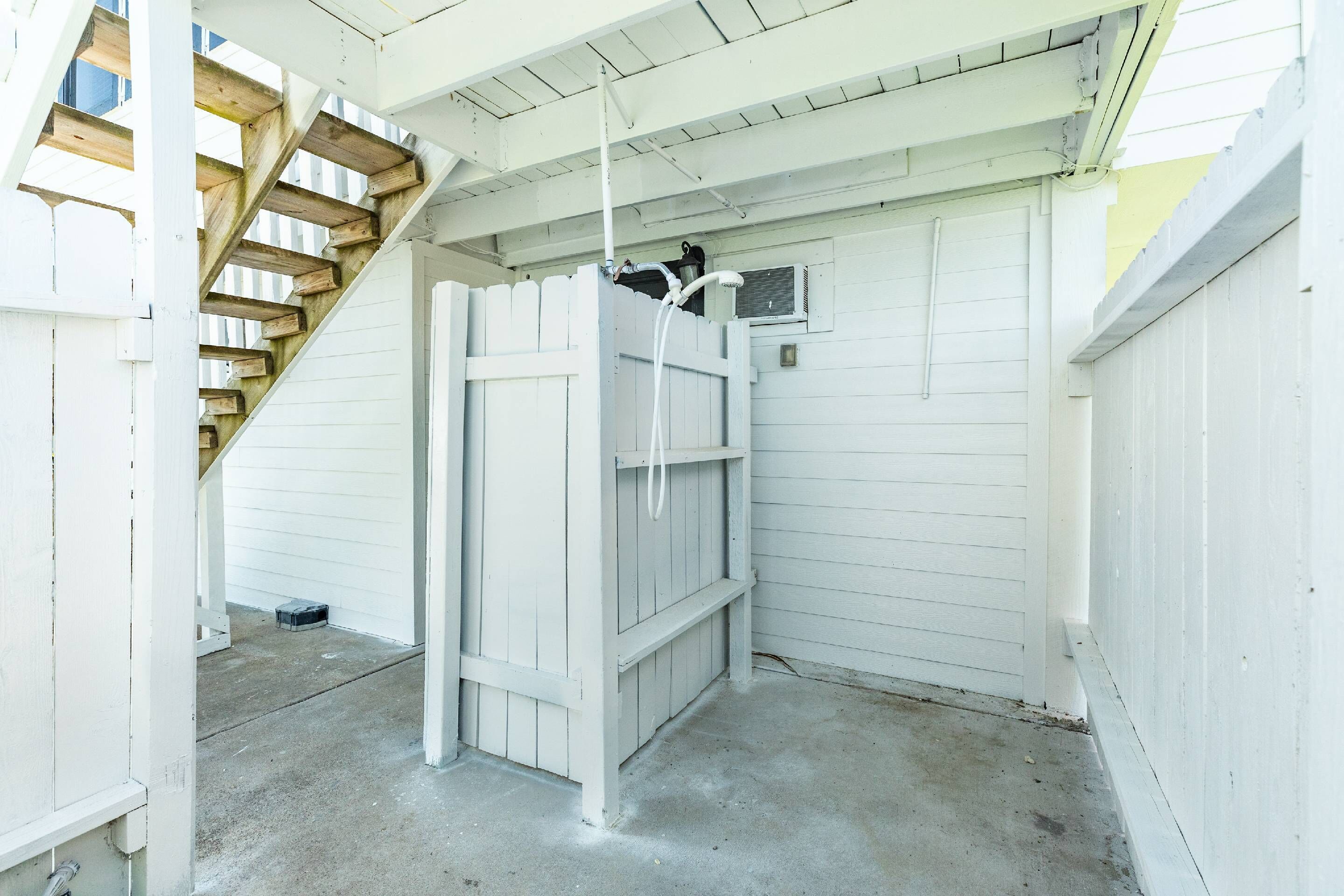 A white wooden structure with a concrete floor, a wooden staircase, and a small window.