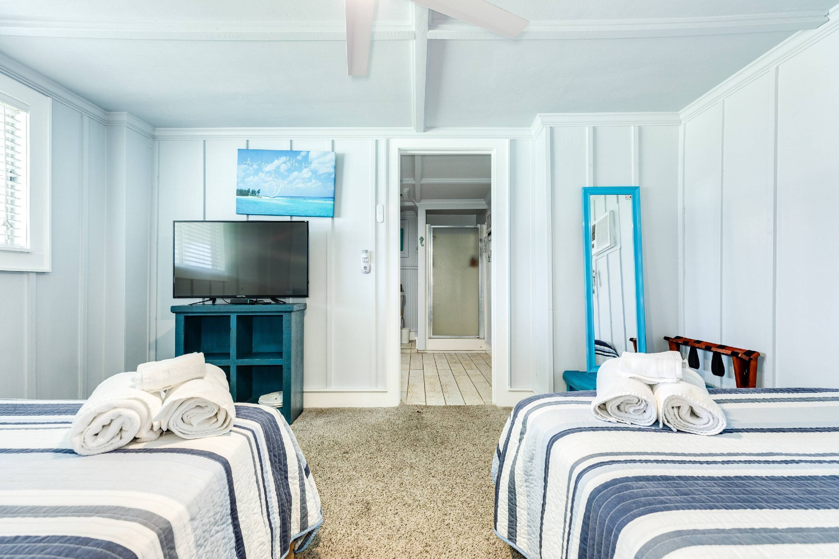 A hotel room with two beds, a TV, a mirror, and a door leading to a hallway.