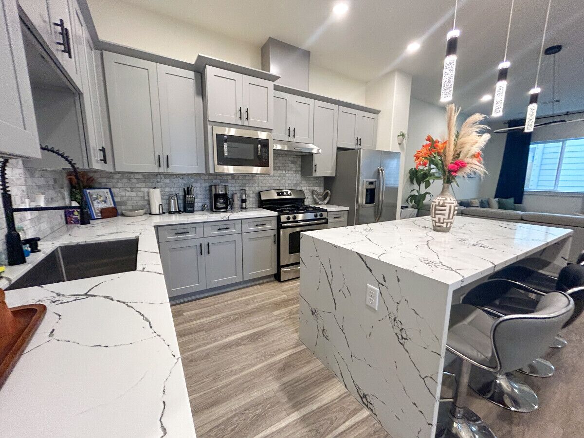 A modern kitchen with grey cabinets, a central island, stainless steel appliances, and a dining area with bar stools.