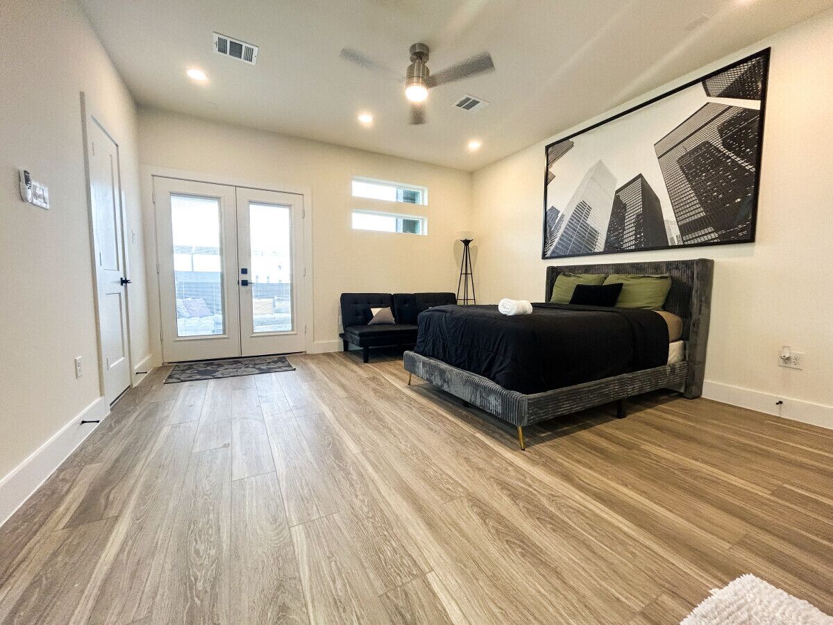 A bedroom with a bed, a ceiling fan, a floor lamp, and a large window.