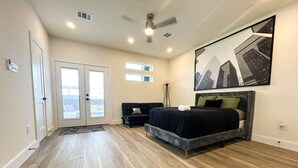 A bedroom with a bed, a ceiling fan, a floor lamp, and a large window. - 4 BR Townhome w/ Rooftop + Skyline View (Houston)