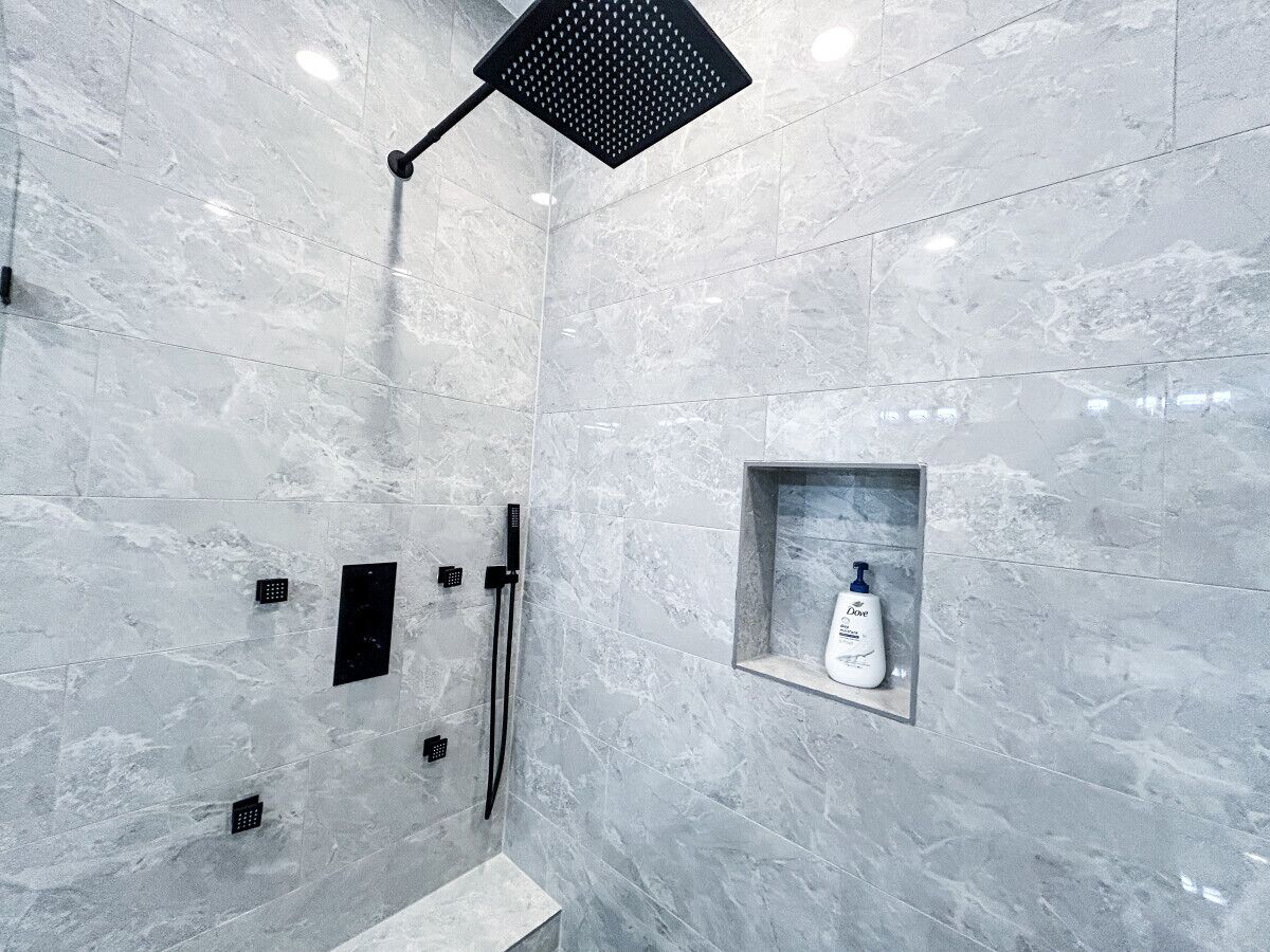 Un baño moderno con pared de mármol, un cabezal de ducha de mano, una ducha de mano y un dispensador de jabón.