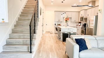 A modern kitchen with a central island, stainless steel appliances, and a staircase with a railing.