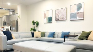 A modern living room with a sectional sofa, a small table, and abstract wall art. - 4 BR Townhome w/ Rooftop + Skyline View (Houston)