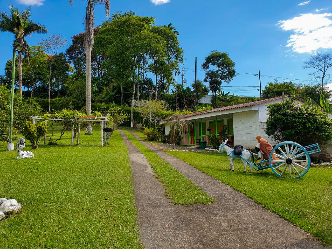 A pathway leading to a white house with a porch, surrounded by lush greenery and a decorative cart.