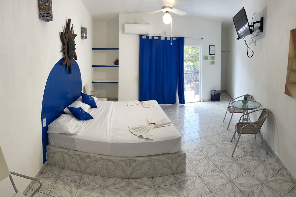 Ein Hotelzimmer mit einem Bett, einem kleinen Tisch mit Stühlen, einem Deckenventilator und einem an der Wand befestigten Fernseher.