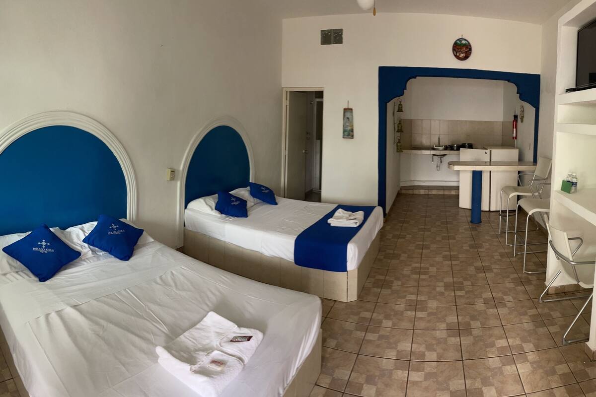 Ein Hotelzimmer mit zwei Betten, einer Küchenzeile und einem Essbereich.