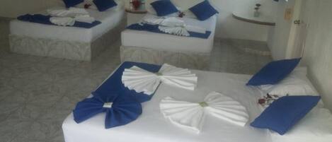 Habitación de hotel con tres camas, cada una con almohadas azules y ropa de cama blanca.